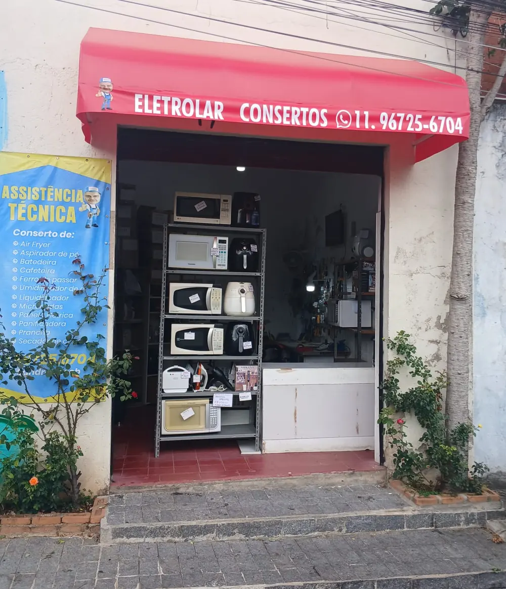 Fachada da Eletrolar: toldo vermelho com o nome da loja e o telefone sobre a porta aberta, com prateleiras de eletrodomésticos ao fundo